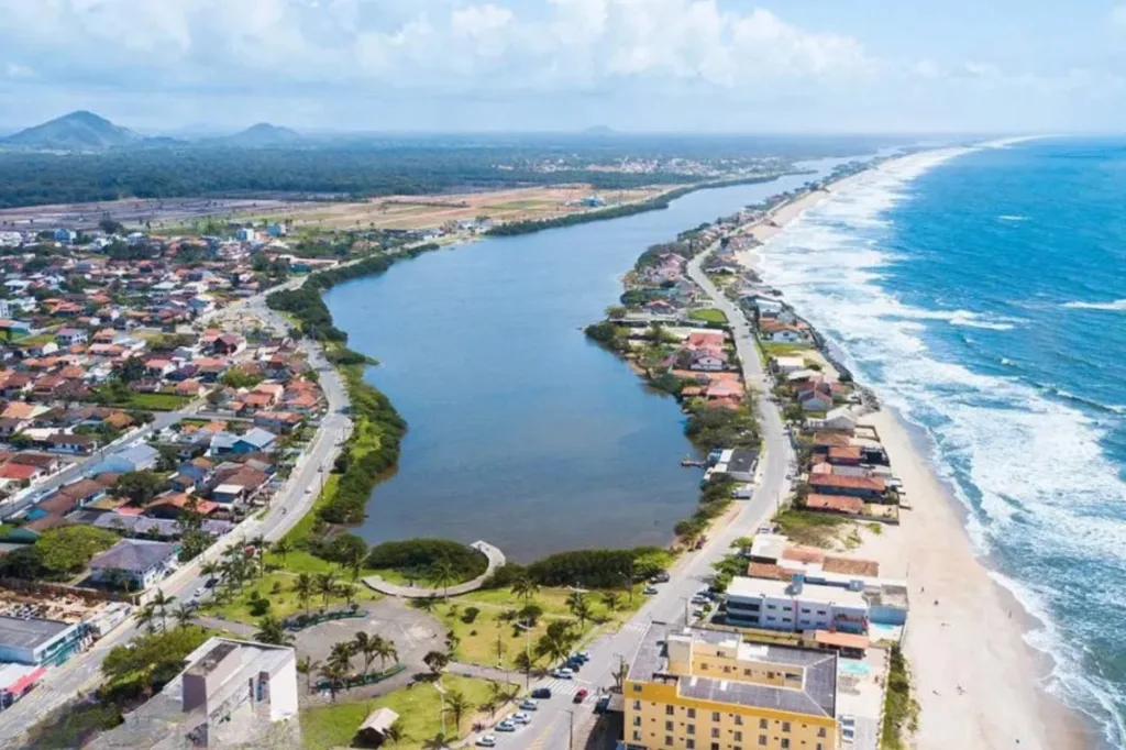 Foto aérea de Barra Velha SC mostrando a lagoa separada do mar por faixa de areia, orla com casas baixas e praia extensa no litoral norte catarinense