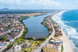 Foto aérea de Barra Velha SC mostrando a lagoa separada do mar por faixa de areia, orla com casas baixas e praia extensa no litoral norte catarinense